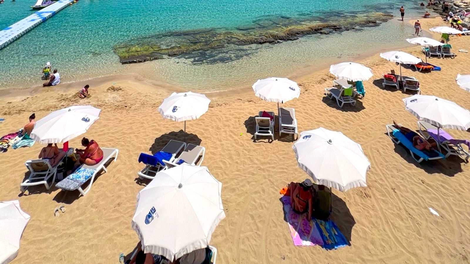 Turquoise shallows and pale golden sand on the Famagusta coast of Cyprus, with sunbeds along the waterline and rocky headlands in the distance